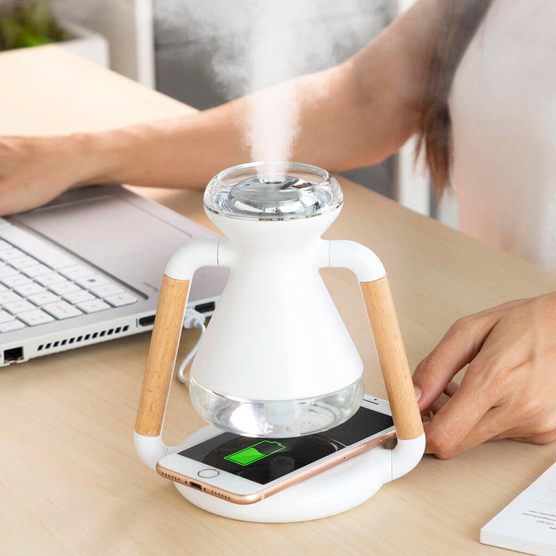 Vista frontal del humidificador difusor de aromas 3 en 1 sobre una mesa minimalista, emitiendo una fina niebla y con un smartphone apoyado en la base.